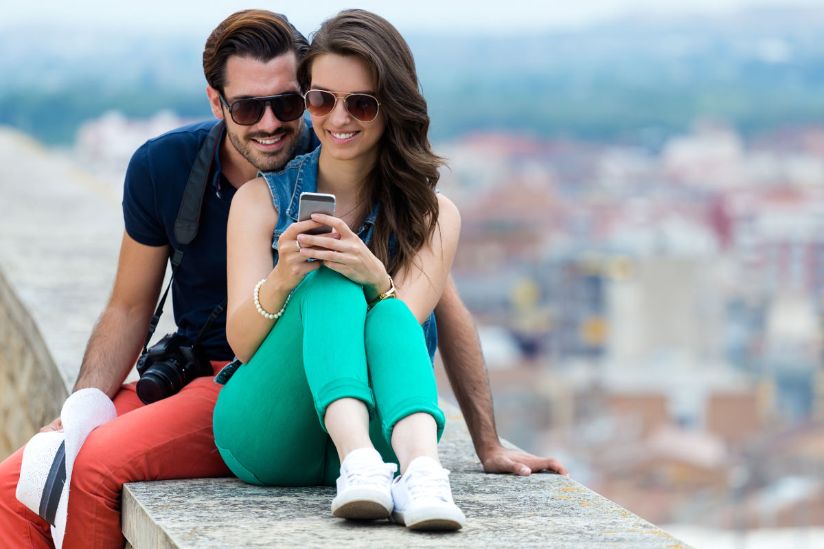 Portrait of young couple of tourist in town using mobile phone.