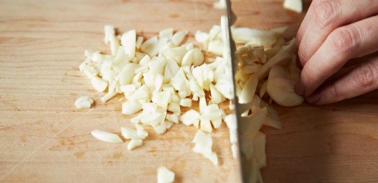 Person mincing garlic on wood cutting board