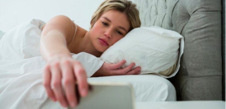 sleepy woman reaching for her phone in bed