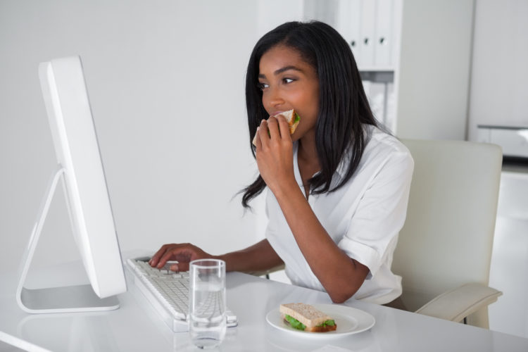 Image of businesswoman eating a sandwich at her desk in her office