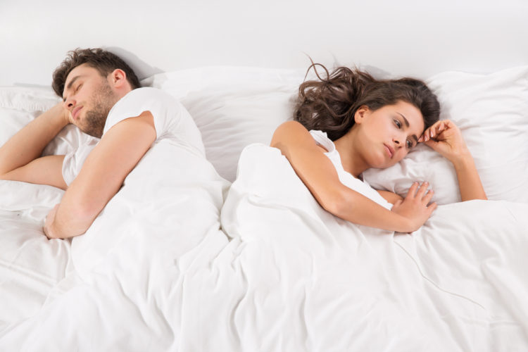 Image of upset young couple having disagreement lying side by side in bed facing in opposite directions