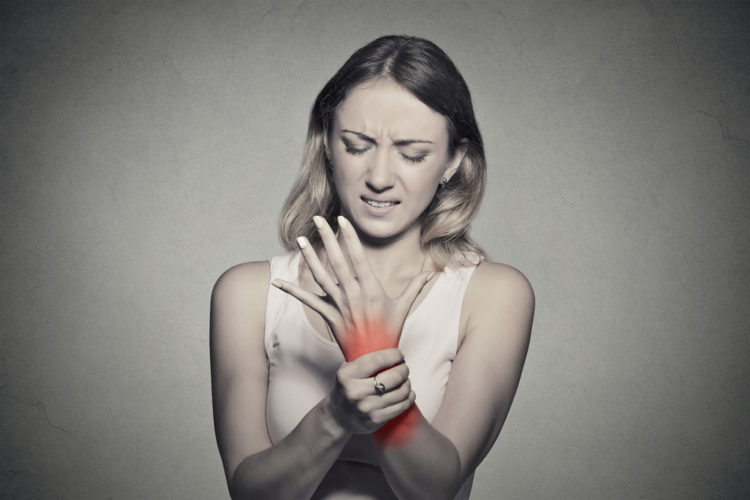Image of young woman holding her painful wrist isolated on gray wall background.