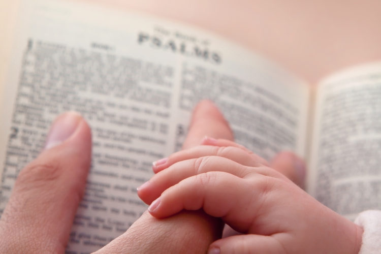 Image of baby holding father’s finger as he points to Psalms verse