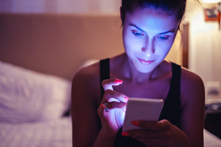 Image of girl looking at mobile phone in the dimmed bedroom