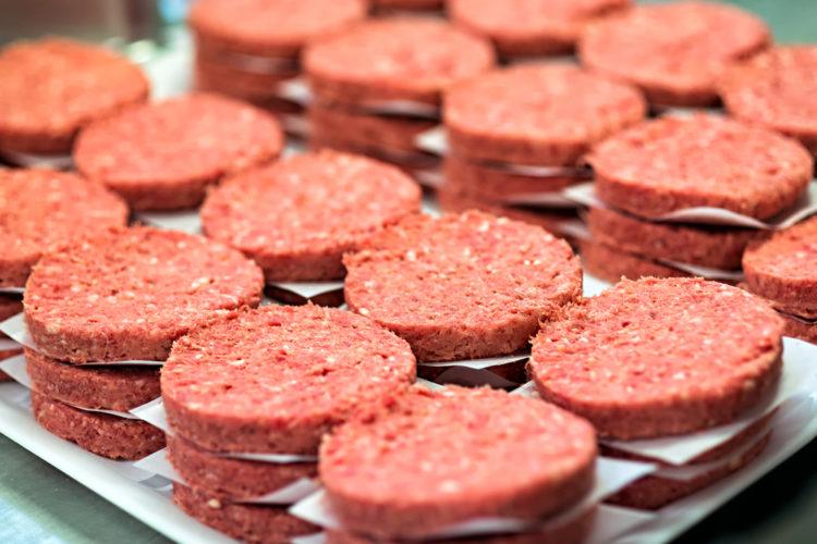 Multiple stacks of freshly processed raw hamburger patties on display in meat processing plant