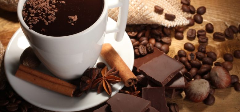 Image of cup of hot chocolate, cinnamon sticks, nuts and chocolate on wooden table