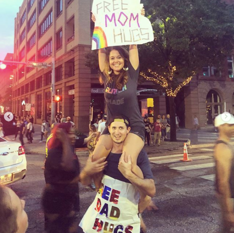 Image of woman and man holding signs that say mom hugs and dad hugs