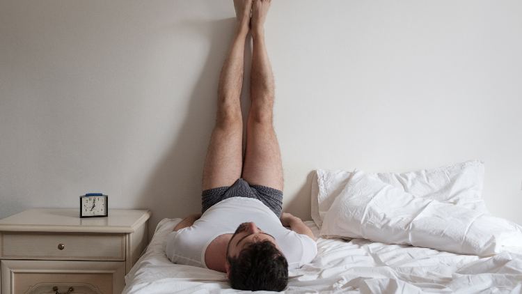 Man stretches muscles on the bed in the bedroom in the morning