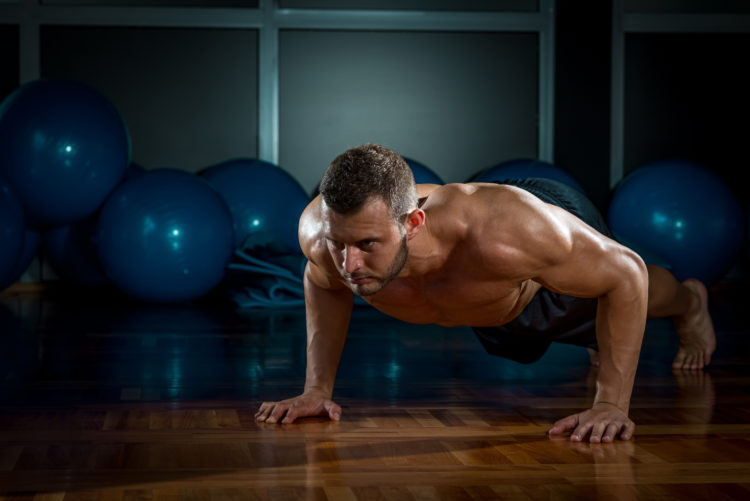 Image of Young adult man doing push-ups in gym.
