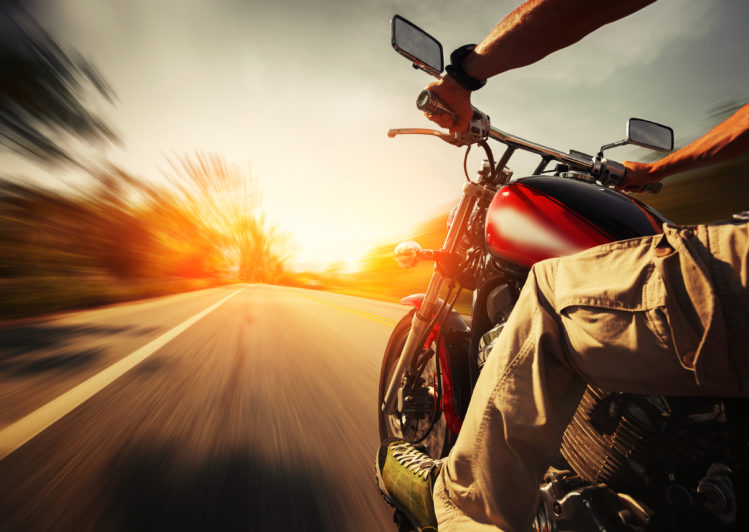 Image of Biker riding motorcycle on an empty road at sunny day