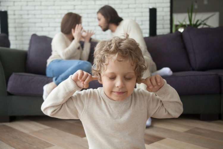 Image of Little boy puts fingers in ears not to hear parents fighting at background, upset tired son suffering from mom and dad arguing, parental conflicts hurt kid, family divorce effect on children concept
