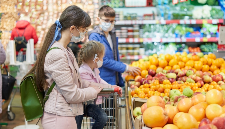 Mom with children in protective masks choose fruits to buy in the store.